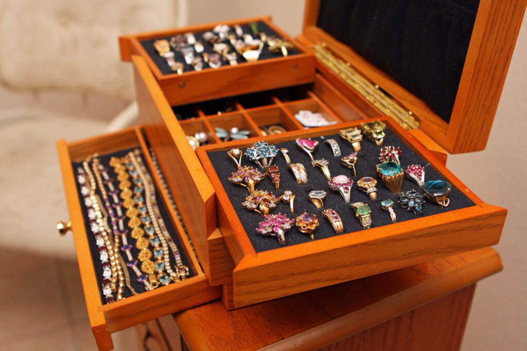 Many multi-colored bracelets and rings with gemstones in a wood jewelry box