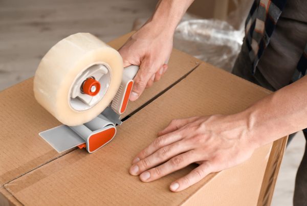 Young man packing moving box indoors, closeup
